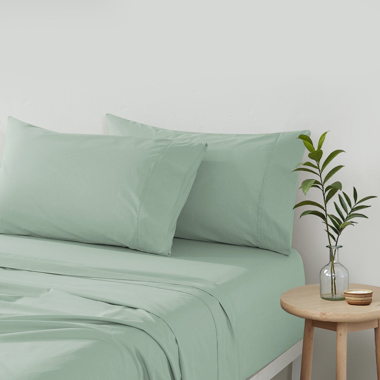sage green cotton percale sheet set on bed with pillows and bedside table